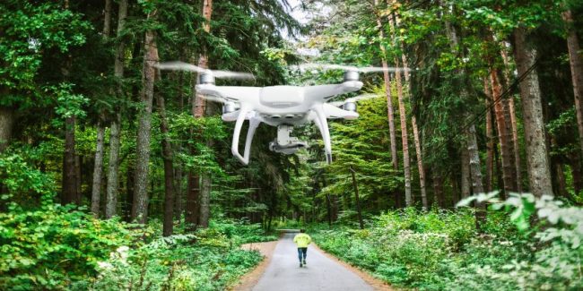 Hovering drone taking pictures of man running in forest.